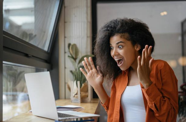 Young Excited African American woman win online lottery, celebration success. Happy emotional female using laptop computer shopping online